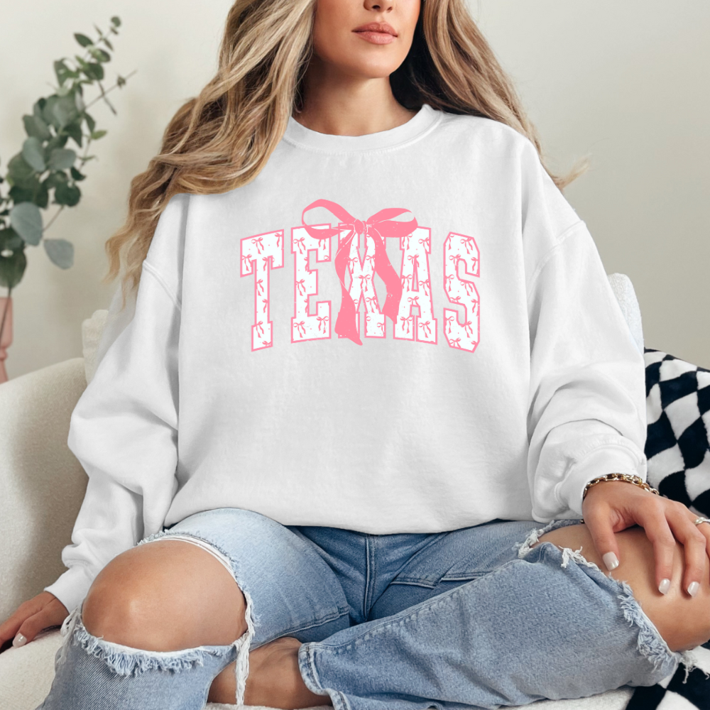 Graphic Texas letters with pink and white bows within texas letters. Cute pink bow centered above X in texas. Chic modern design. White Sweater