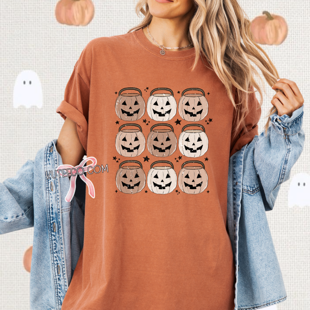 Person wearing a burnt orange t-shirt with Halloween-themed design, jack o lantern pumpkin buket 9 in rows  with dainty black stars around as accents.