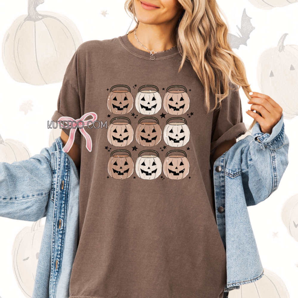 Person wearing a espresso brown t-shirt with Halloween-themed design, jack o lantern pumpkin bucket 9 in rows  with dainty black stars around as accents.