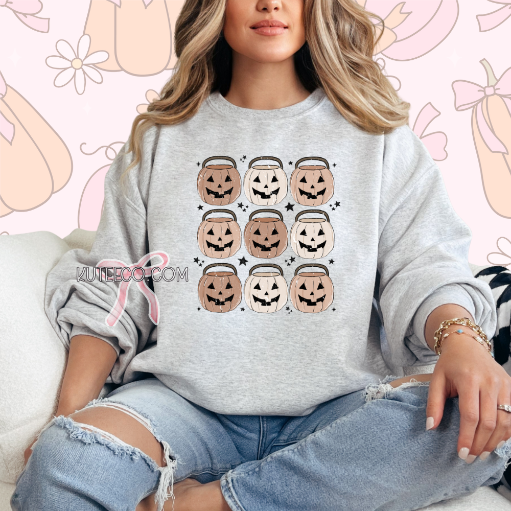 Person wearing a light gray sweatshirt with Halloween design, jack o lantern pumpkin buckets 9 in rows with dainty black stars around as accents.