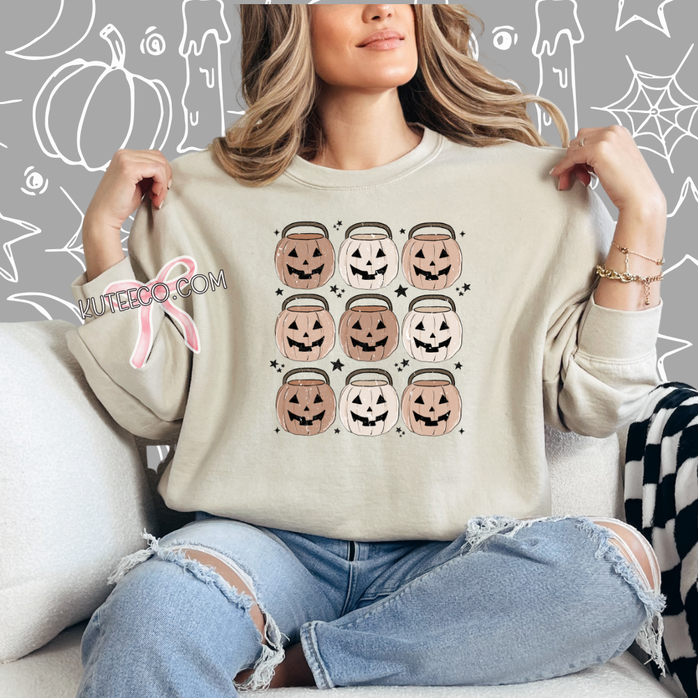 Person wearing a beige sweatshirt with Halloween design, jack o lantern pumpkin buckets 9 in rows with dainty black stars around as accents.