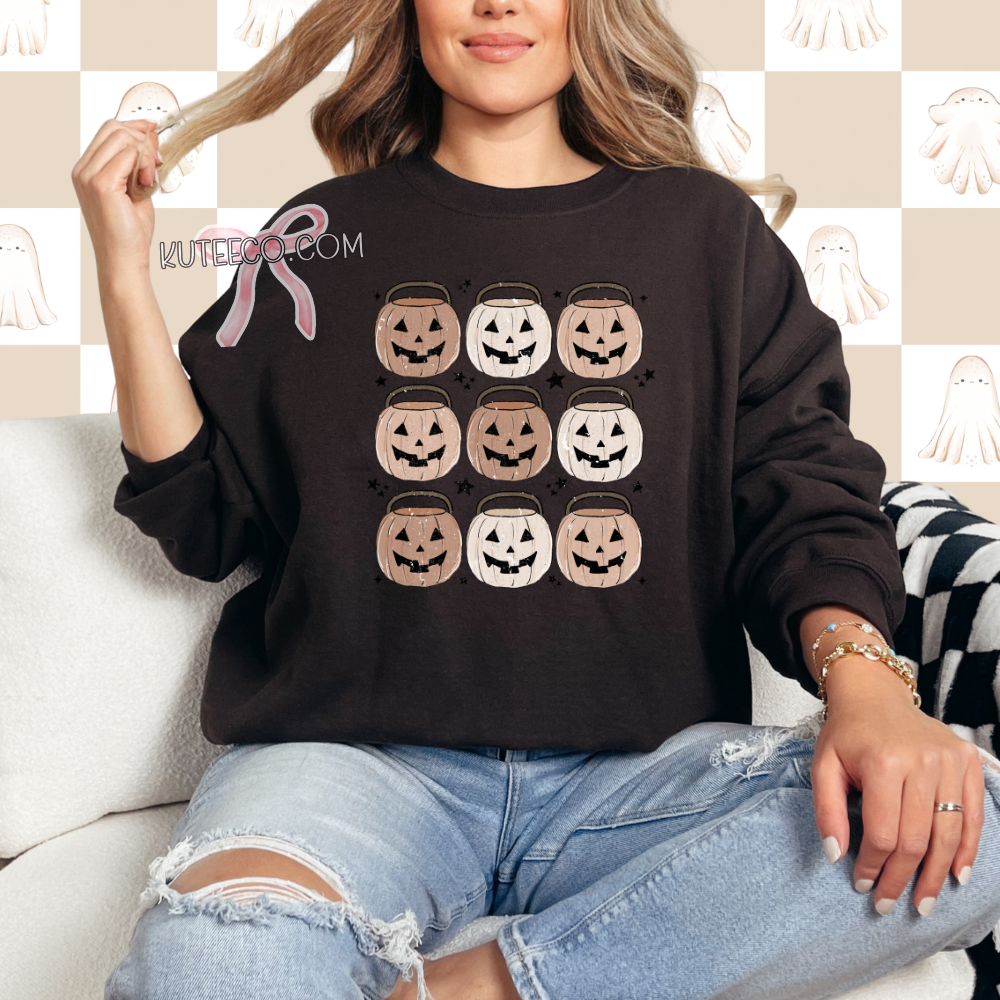 Person wearing a brown sweatshirt with Halloween design, jack o lantern pumpkin buckets 9 in rows with dainty black stars around as accents.